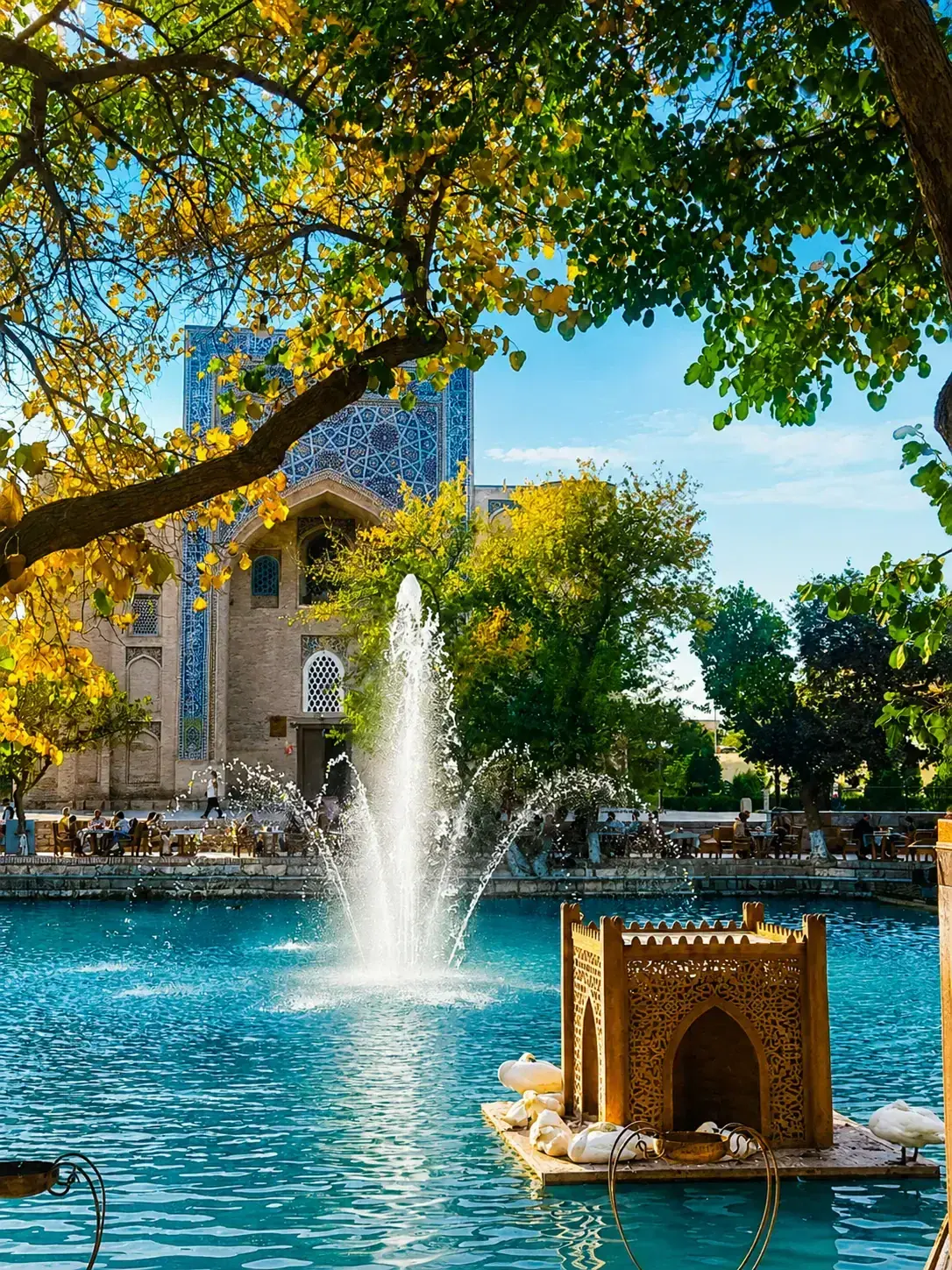 Fontein in een turquoise bassin voor een historisch gebouw met blauwe tegelmozaïeken, omzoomd door bomen