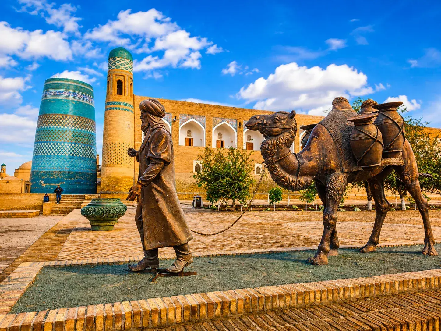 Bronzen beeld van een karavaanleider met kameel voor de blauwe Kalta Minor minaret in Khiva, Oezbekistan