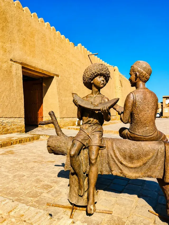 Bronzen beelden van kinderen voor een historische lemen stadsmuur